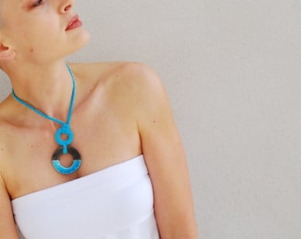 May include: A woman wearing a white strapless top with a blue and black pendant necklace. The pendant is a large circle with a smaller circle inside.