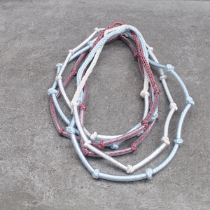 May include: Three intertwined necklaces made of braided rope. The necklaces are in shades of blue, white, and pink.