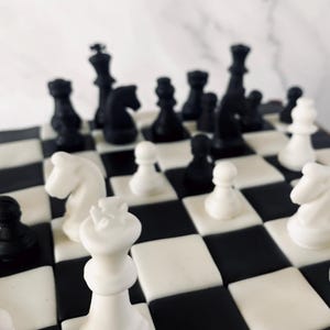Könnte beinhalten: Nahaufnahme eines Schachbretts mit schwarzen und weißen Figuren. Die Figuren umfassen Könige, Damen, Türme, Springer und Bauern. Das Brett hat ein klassisches schwarz-weißes Schachmuster. Die Figuren sind wie mitten in einem Spiel angeordnet.
