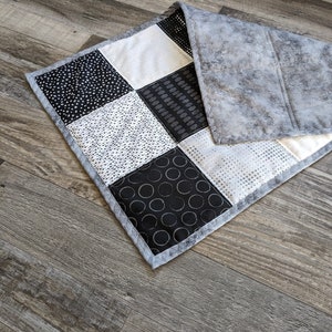 May include: A black and white patchwork quilt with a gray backing. The quilt is made of different fabrics with geometric patterns.
