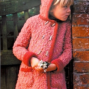 May include: A pink hooded coat with red trim and toggle closures. The coat has a textured, fuzzy appearance and is worn by a child. The child is holding a small bouquet of white flowers. The coat has pockets and ribbed cuffs.
