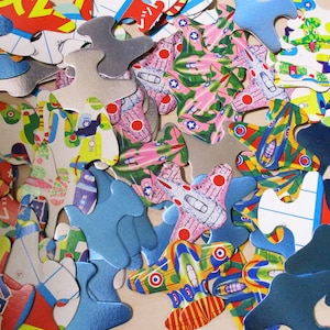 May include: A collection of colorful jigsaw puzzle pieces with various designs, including airplanes, flowers, and geometric patterns. The pieces are made of cardboard and have a glossy finish.
