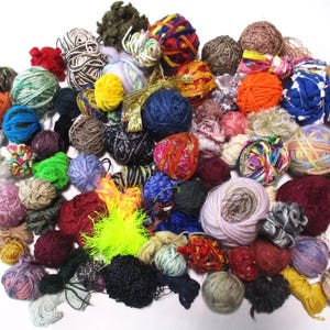 May include: A large collection of colorful yarn balls in various textures and patterns. The yarn is arranged in a random pattern on a white surface.