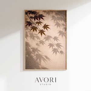 Puede incluir: Impresión enmarcada de hojas de arce y sus sombras. Las hojas son de color marrón cálido, con sombras más oscuras sobre un fondo neutro. La impresión incluye el texto "AVORI STUDIO" en la parte inferior y está en un marco de madera.