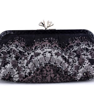 Peut inclure: Pochette noire avec un fermoir argenté et un motif de dentelle décoratif. La pochette présente une sangle noire et un motif de dentelle florale détaillé en argent et gris foncé.