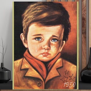 Könnte beinhalten: Gerahmter Druck eines Kindes mit blauen Augen, das weint. Das Kind trägt einen beigefarbenen Mantel und einen roten Schal. Der Druck zeigt den Text "1950" und zwei Sterne in der unteren rechten Ecke.