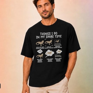 May include: A black t-shirt featuring white text and graphics that read: THINGS I DO IN MY SPARE TIME, with illustrations of bearded dragons and captions: HANG OUT WITH BEARDED DRAGONS, LOOK AT BEARDED DRAGONS, RESEARCH BEARDED DRAGONS, TALK ABOUT BEARDED DRAGONS, THINK ABOUT BEARDED DRAGONS, DREAM ABOUT BEARDED DRAGONS.
