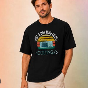 May include: A black short-sleeve t-shirt featuring a graphic with a retro sunset design in yellow, orange, and red. The graphic includes a keyboard illustration and the text "JUST A BOY WHO LOVES <CODING/>" in a white, pixelated font style.