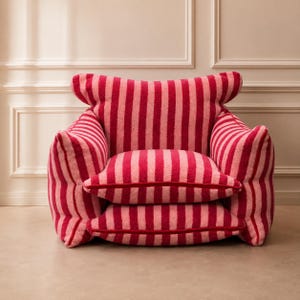 May include: An armchair upholstered in a textured, fuzzy fabric featuring vertical stripes in alternating shades of deep red and light pink. The chair has a wide, rounded backrest, two thick armrests, and two stacked, plush seat cushions.