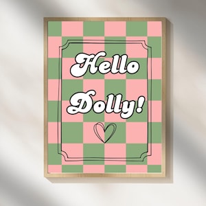 Puede incluir: Un estampado enmarcado con un fondo a cuadros rosa y verde. Las palabras "Hello Dolly!" están en blanco, con una fuente estilizada y un pequeño corazón debajo. El marco es de color madera clara.