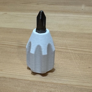 May include: A white 3D-printed screwdriver handle with a black Phillips head bit. The handle has a textured, ridged design for grip and is sitting on a wooden surface.