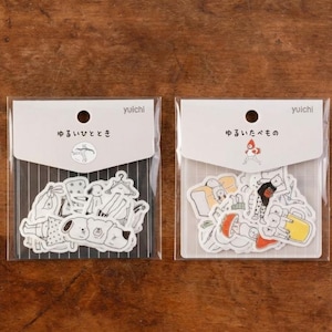 Puede incluir: Dos paquetes de pegatinas con ilustraciones de personas y objetos. Un paquete presenta ropa y un perro, el otro muestra comida y una persona. Cada paquete está en una funda de plástico transparente con texto japonés y un logotipo circular.