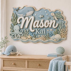 Könnte beinhalten: Ein hölzernes Wandschild mit dem Namen Mason Kai in weißer Schreib- und Blockschrift. Das Design zeigt mehrschichtige Ausschnitte eines Blauwals, einer grünen Meeresschildkröte, eines Oktopus, Seesternen, Muscheln und verschiedenen Fischen in Meeresfarben.