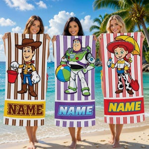 Puede incluir: Tres toallas de playa con los personajes de Toy Story Woody, Buzz Lightyear y Jessie. Cada toalla tiene una ilustración de personaje sobre un fondo a rayas con una sección "NAME" personalizada en la parte inferior. Las toallas se sostienen en una playa.