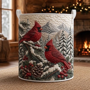 May include: A cylindrical quilted fabric storage basket featuring a winter scene with two bright red cardinals perched on snow-covered pine branches. The design includes pinecones, red berries, and a backdrop of snowy mountains and evergreen trees.