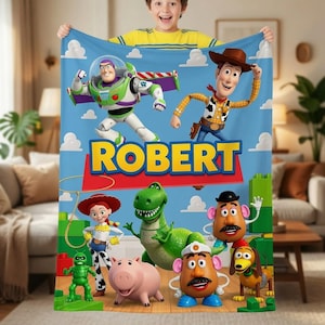 Puede incluir: Una manta de forro polar azul con personajes de Toy Story como Buzz Lightyear, Woody, Jessie, Rex, Hamm, el Sr. Patata y Slinky Dog. El nombre ROBERT est&aacute; impreso en letras amarillas grandes sobre un fondo rojo en el centro.