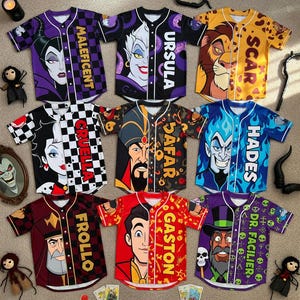 May include: Collection of baseball jerseys featuring various Disney villains. Each jersey has a character's face on the front, with names like Maleficent, Ursula, Scar, and Hades. The jerseys are in various colors, including purple, black, and red.