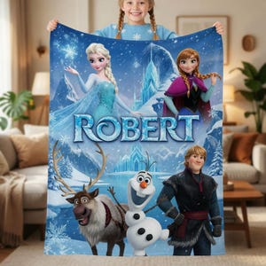 May include: A blue fleece blanket featuring the characters Elsa, Anna, Kristoff, Sven, and Olaf from Frozen, with the name ROBERT printed in large blue letters across the center against a snowy mountain landscape with snowflakes.