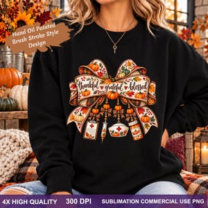 May include: A black crewneck sweatshirt featuring a large graphic of a decorative bow adorned with autumn leaves and pumpkins. The text "thankful grateful blessed" is centered on the bow, which hangs over medical icons including a clipboard, syringe, nurse cap, and pill bottle.