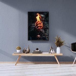 May include: Framed artwork featuring a person holding a fiery object. The image has a dark, dramatic aesthetic. The person is wearing a necklace with a pendant. The artwork is displayed above a wooden table with decorative items.