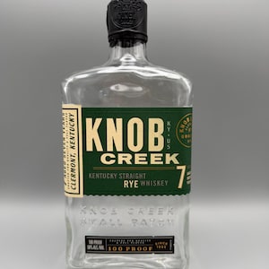 May include: An empty clear glass bottle of Knob Creek Kentucky Straight Rye Whiskey with a dark green label. The label features the text Knob Creek, 7, and Clermont, Kentucky. The bottle has a black cap and embossed text reading Knob Creek Small Batch.