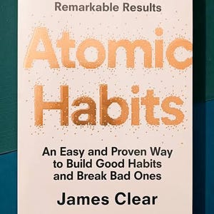 May include: A book titled "Atomic Habits" with the subtitle "An Easy and Proven Way to Build Good Habits and Break Bad Ones" by James Clear. The cover is off-white with orange text and a dotted pattern.