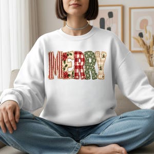 May include: A white long-sleeve sweatshirt featuring the word MERRY printed across the chest. Each letter has a distinct pattern, including red and white stripes, poinsettia florals, red and white gingham, green foliage, and a beige plaid.