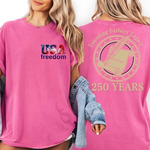 A woman wearing a pink t-shirt with the text "USA freedom" and "250 years" printed on it, along with a graphic of a feather quill and a document.
