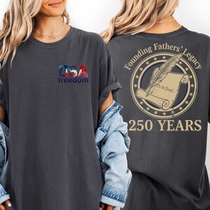 a woman wearing a black t-shirt with a graphic design on the back. The design includes the text "USA freedom" and "Founding Fathers' Legacy" along with a feather and a scroll.