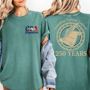 A woman wearing a green t-shirt with the text "USA freedom" and "Founding Fathers' Legacy" printed on it, along with a graphic of a feather and a scroll.