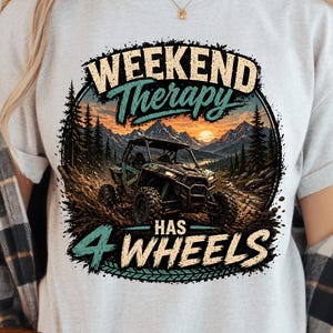 May include: Pale grey t-shirt featuring the text "WEEKEND Therapy HAS 4 WHEELS" with a graphic of a four-wheel drive vehicle in a forest setting. The design includes a sunset and a "PNG" logo. The words "Instant Download" are also visible.