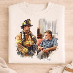 May include: A cream-coloured sweatshirt with a watercolour illustration. It depicts a firefighter in uniform and an older man in a blue shirt. The firefighter wears a helmet and gear. The older man is seated in a chair. The design is split down the middle.