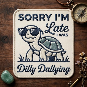 May include: Embroidered patch with a cartoon turtle wearing sunglasses. The patch reads "SORRY I'M Late I WAS Dilly Dallying" in navy blue script. The patch is rectangular with rounded corners and is on a wooden surface.