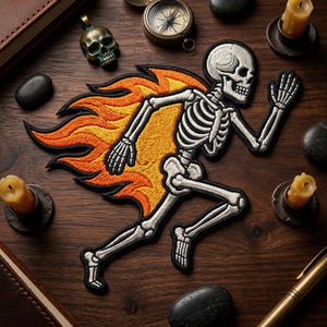 May include: Embroidered patch featuring a running skeleton with flames. The skeleton is white with black detailing, and the flames are orange and yellow. The patch is on a dark brown wooden surface, with other objects like a compass and candles.