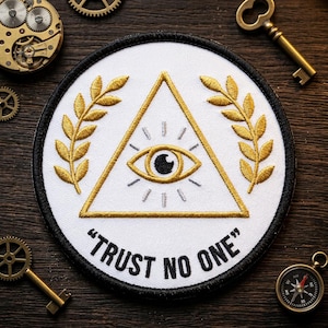 May include: Embroidered patch with a white background, black border, and the text "TRUST NO ONE." The patch features a gold triangle with an eye, surrounded by gold laurel branches. The design is circular.