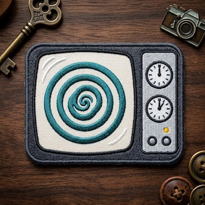 May include: Embroidered patch featuring a retro television design. The TV screen displays a teal spiral, with two clock faces on the side. The patch has a dark gray border and is set against a wooden background.