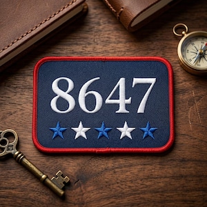 May include: A navy blue patch with the number "8647" in white, and five stars, two blue and three white. The patch has a red border. A compass, key, and leather-bound notebook are in the background.