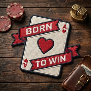 May include: Embroidered patch featuring a playing card design with a red heart and the text "BORN TO WIN" on a red banner. The patch is on a wooden surface with poker chips, dice, and a leather card holder.