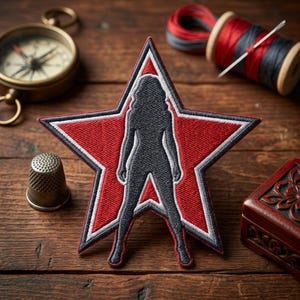 May include: Embroidered patch featuring a silhouette of a woman within a red star with white and black trim. The patch is on a wooden surface, with a compass, thimble, thread spools, and a small wooden box in the background.