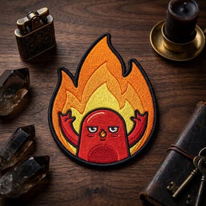 May include: Embroidered patch featuring a red cartoon character engulfed in flames. The character has a grumpy expression and is giving the finger. The patch is outlined in black and has yellow and orange flames.