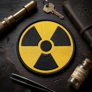 May include: Yellow and black radiation symbol patch. The patch features a black trefoil symbol on a yellow background. Other items include a key, a small telescope, a glass bottle labeled "Radioactive - 1947", and a leather-bound journal.