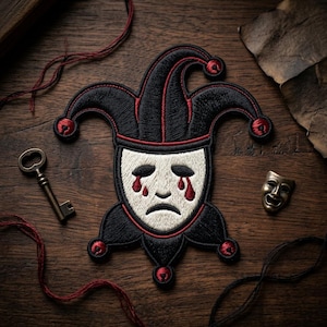 May include: Embroidered patch featuring a jester design with a black and red color scheme. The jester has a white face with red teardrops. A small key and a smiling mask are also present on a wooden surface.
