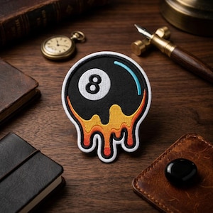 May include: A black and white embroidered patch featuring the number 8 inside a white circle, with a blue arc and orange and yellow dripping design. The patch is on a wooden surface.