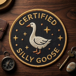 May include: Embroidered patch with a black background and gold trim, featuring a goose illustration and the words "CERTIFIED SILLY GOOSE" in gold. The patch includes gold stars and dots.