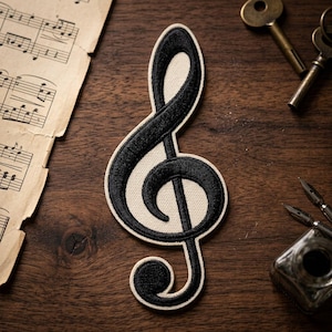 May include: Black treble clef patch with a cream-colored background and black embroidered outline. The patch is on a wooden surface with vintage sheet music, keys, and ink pens. A classic music symbol.
