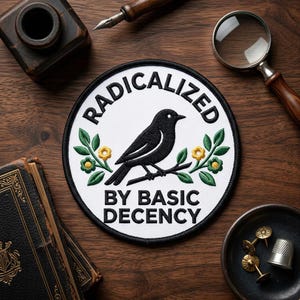 May include: A circular patch with the words "RADICALIZED" and "BY BASIC DECENCY" encircling a black bird perched on a branch with green leaves and yellow flowers. The patch has a white background and a black border.