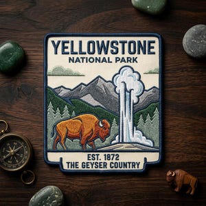May include: Embroidered patch featuring a bison, geyser, and mountains, with the text "YELLOWSTONE NATIONAL PARK" and "EST. 1872 THE GEYSER COUNTRY." The patch has a cream background with a navy blue border and is surrounded by decorative stones and a compass.