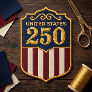 May include: Embroidered patch with the text "UNITED STATES 250" in gold on a blue background. The bottom half features red and white stripes. Gold scissors and thread are visible on a wooden surface.