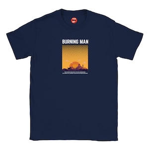 Puede incluir: Camiseta azul marino con un gráfico que presenta el texto "BURNING MAN" sobre una escena de puesta de sol naranja y amarilla con siluetas de edificios y figuras. La camiseta también tiene una cita en la parte inferior.