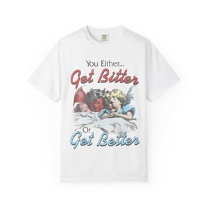 May include: White t-shirt with the text "You Either... Get Bitter Or Get Better" in red and blue. The graphic features a devil and an angel. The devil is red, and the angel is wearing blue.